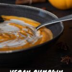 Best creamy vegan pumpkin soup in a dark dish with a spoon.