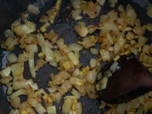 Cooking diced onion in a pot with fresh ginger and aromatic spices.