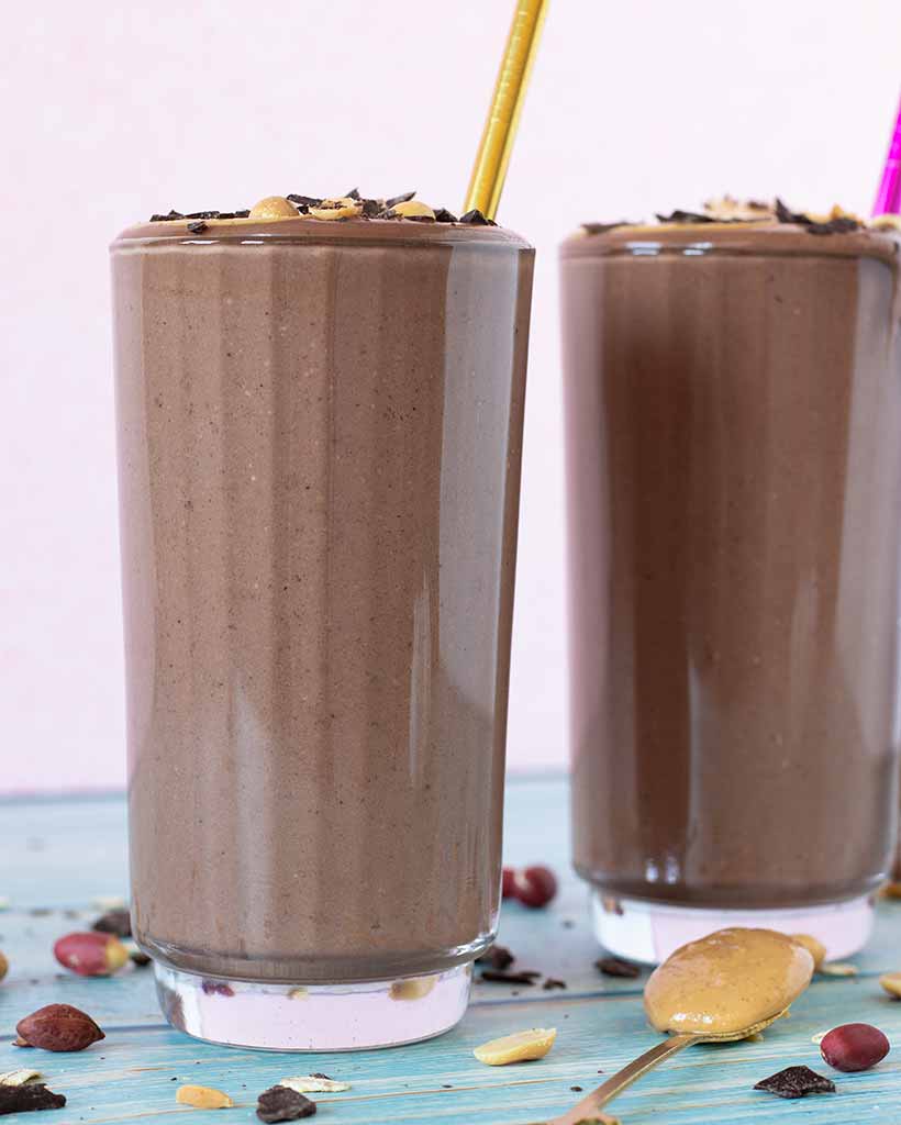 Two glasses of delicious chocolate peanut butter smoothie on blue wooden table as an after workout snack.
