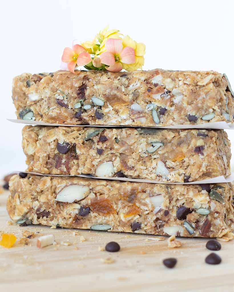 Healthy and chewy vegan granola bars stacked on a wooden board with peanut butter and chocolate chips.
