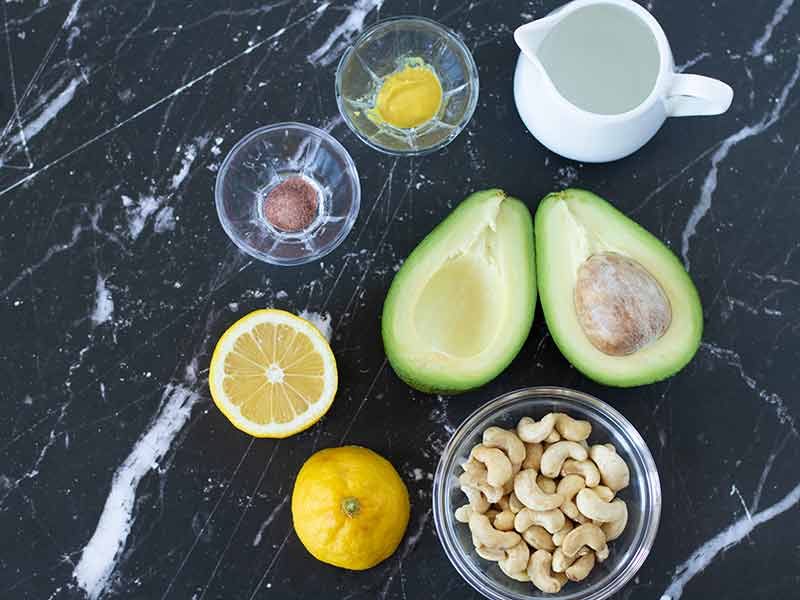 Simple plant-based ingredients for preparing homemade vegan spread: avocado, raw cashews, lemon juice, mustard, spices and water.