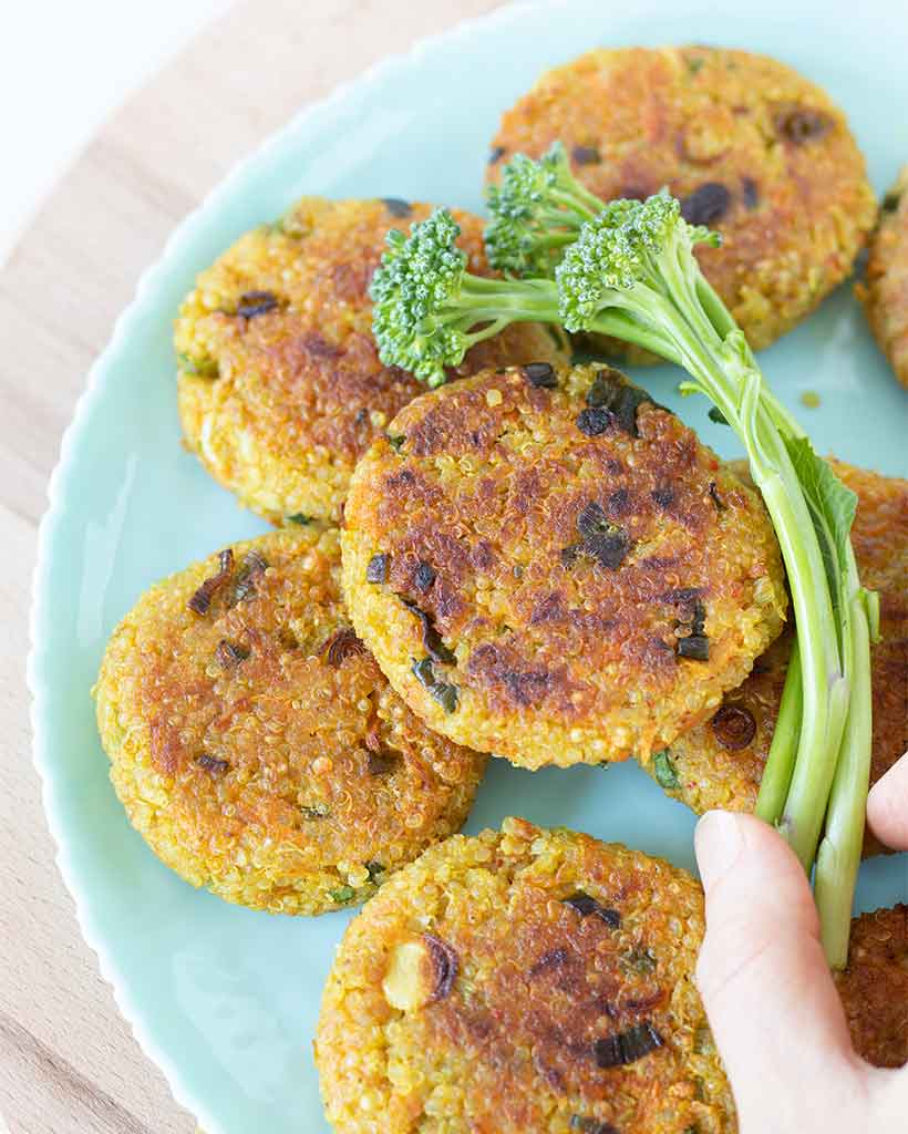 Crispy golden quinoa patties in a light blue plat with fresh broccoli.