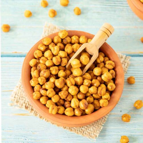 Recipe for roasted chickpeas - spiced crunchy vegan snacks in a plate with wooden spoon on wooden table.