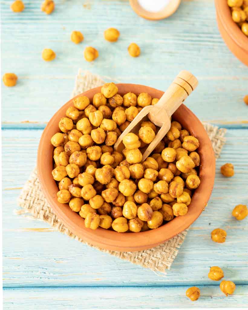 Recipe for roasted chickpeas - spiced crunchy vegan snacks in a plate with wooden spoon on wooden table.