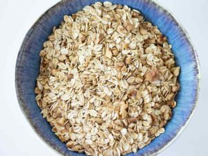 Rolled oats, chopped walnuts, baking soda, ground cinnamon, nutmeg, and salt mixed in a bowl for making peanut butter banana baked oatmeal without sugar.