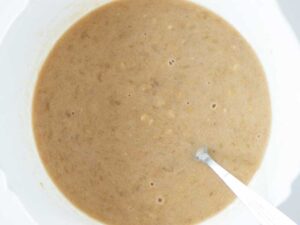 Mashed bananas, peanut butter, maple syrup, pure vanilla extract, and dairy-free milk mixed in a bowl for baking healthy baked oatmeal without eggs.