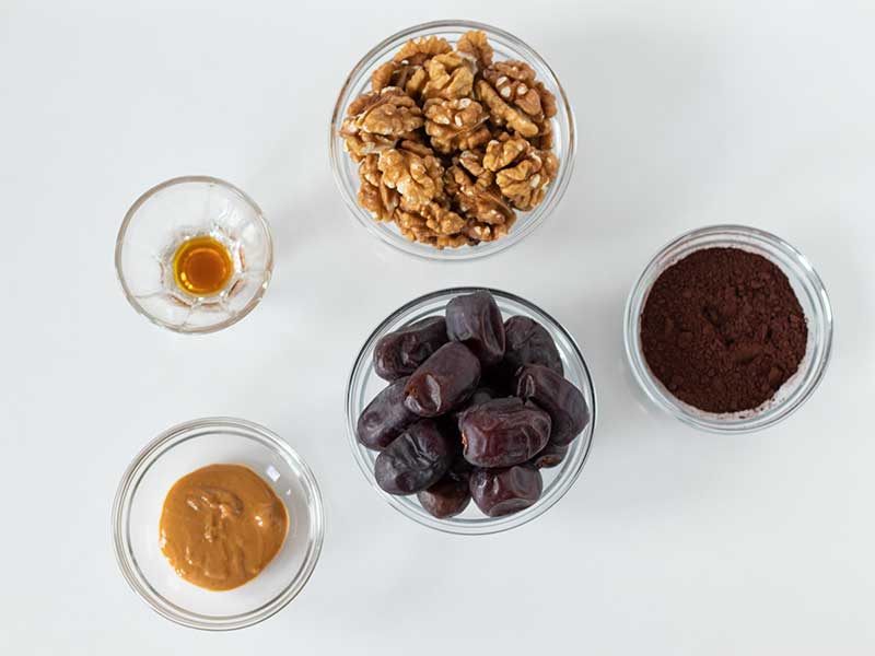 Simple plant-based ingredients for the best recipe for date balls: dates, raw walnuts, unsweetened cacao powder, creamy peanut butter, and pure vanilla extract.