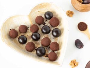 Homemade chocolate date balls in a heart-shaped plate on a white table.