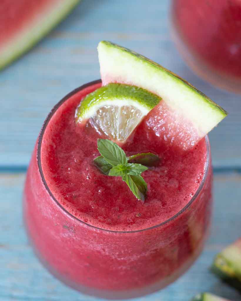 Icy fruity summer drink in a glass decorated with watermelon, fresh mint, and lime