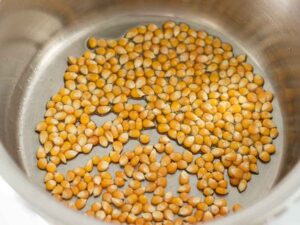 Whole food corn kernels in a heated pot with olive oil for making a quick and easy salty vegan snack