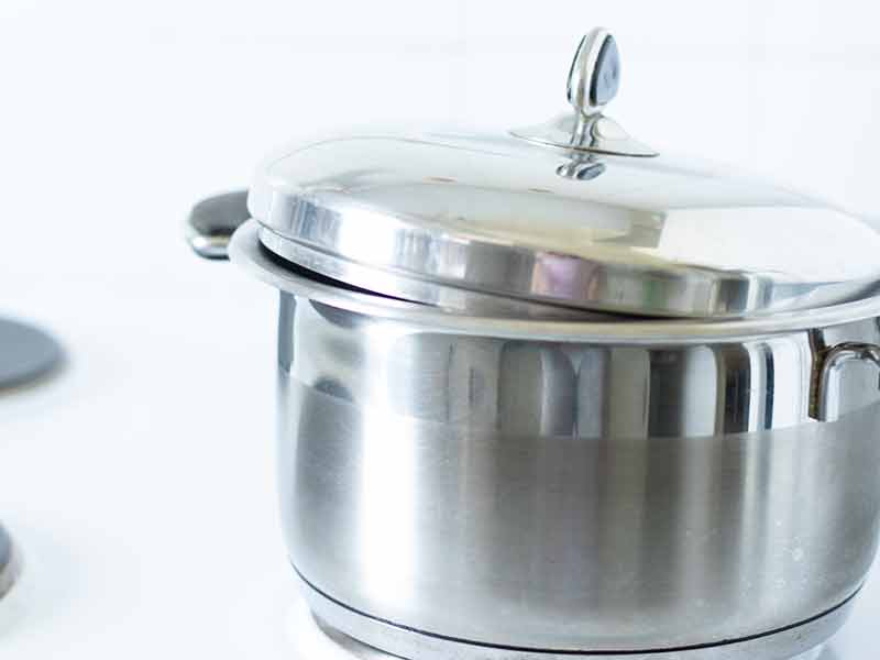 Large stainless steel pot covered with a lid on a stove top for making crispy popcorn at home