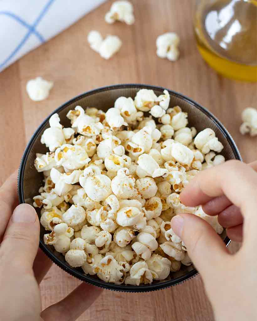 Crunchy homemade popcorn in a bowl with a hand for the best savory vegan snack made at home.