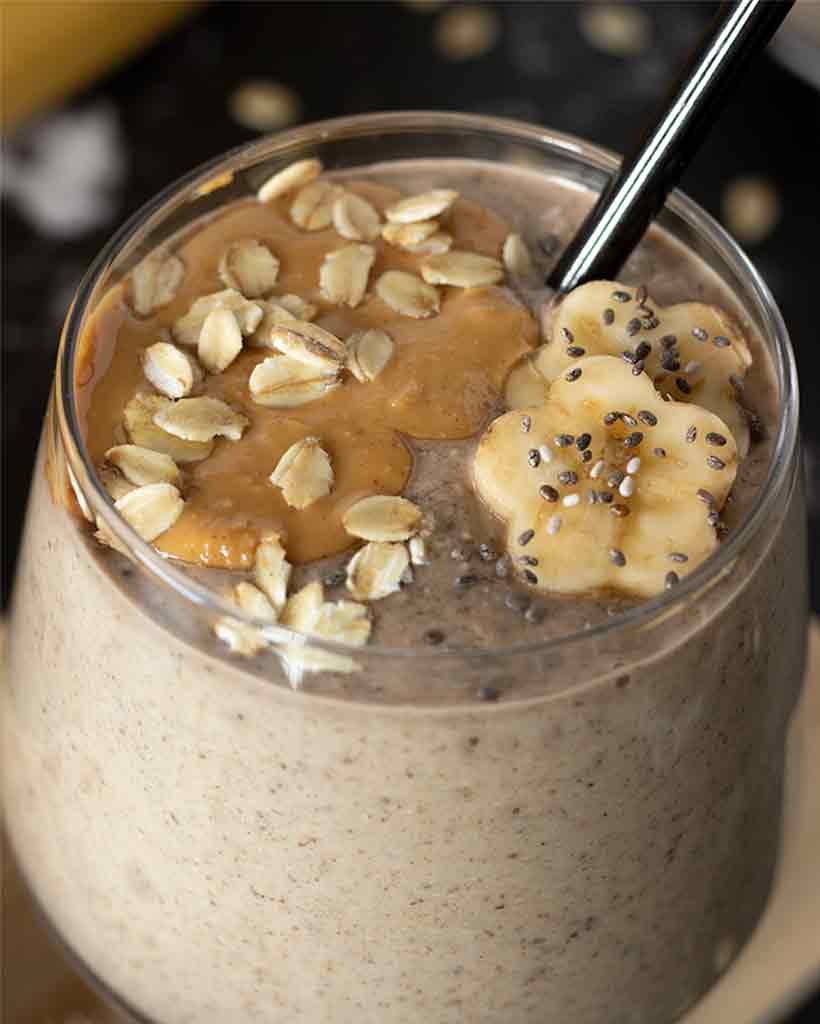 Healthy banana oat smoothie in a glass with black straw