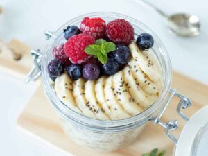 Weightloss overnight oats in a jar topped with raspberries, blueberries, sliced banana, and fresh mint