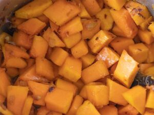 Onion, garlic, chopped butternut squash with spices in a pot for cooking dairy-free soup.