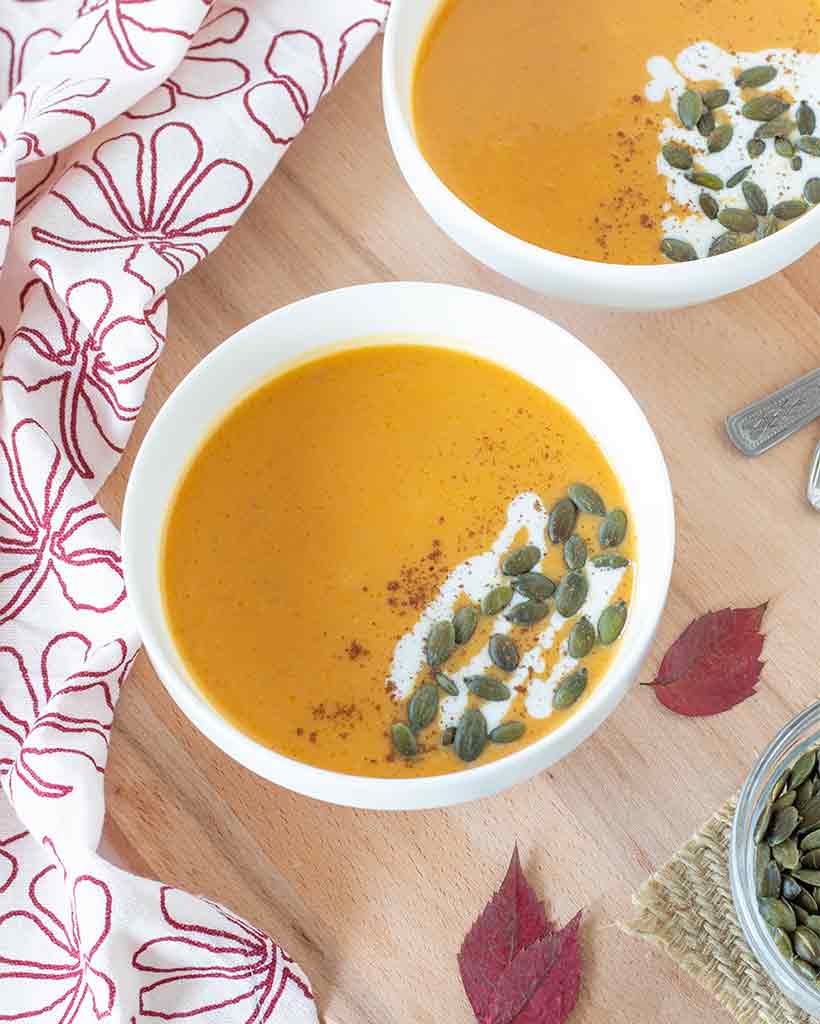 Healthy homemade fall soup in a bowl with toasted pumpkin seeds and dry leaves on a wooden table