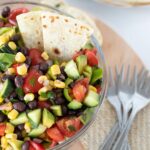 Mediterranean corn salad with black beans in a bowl with homemade torillas placed on a wooden board with forks served as an easy side dish, appetizer, or dinner