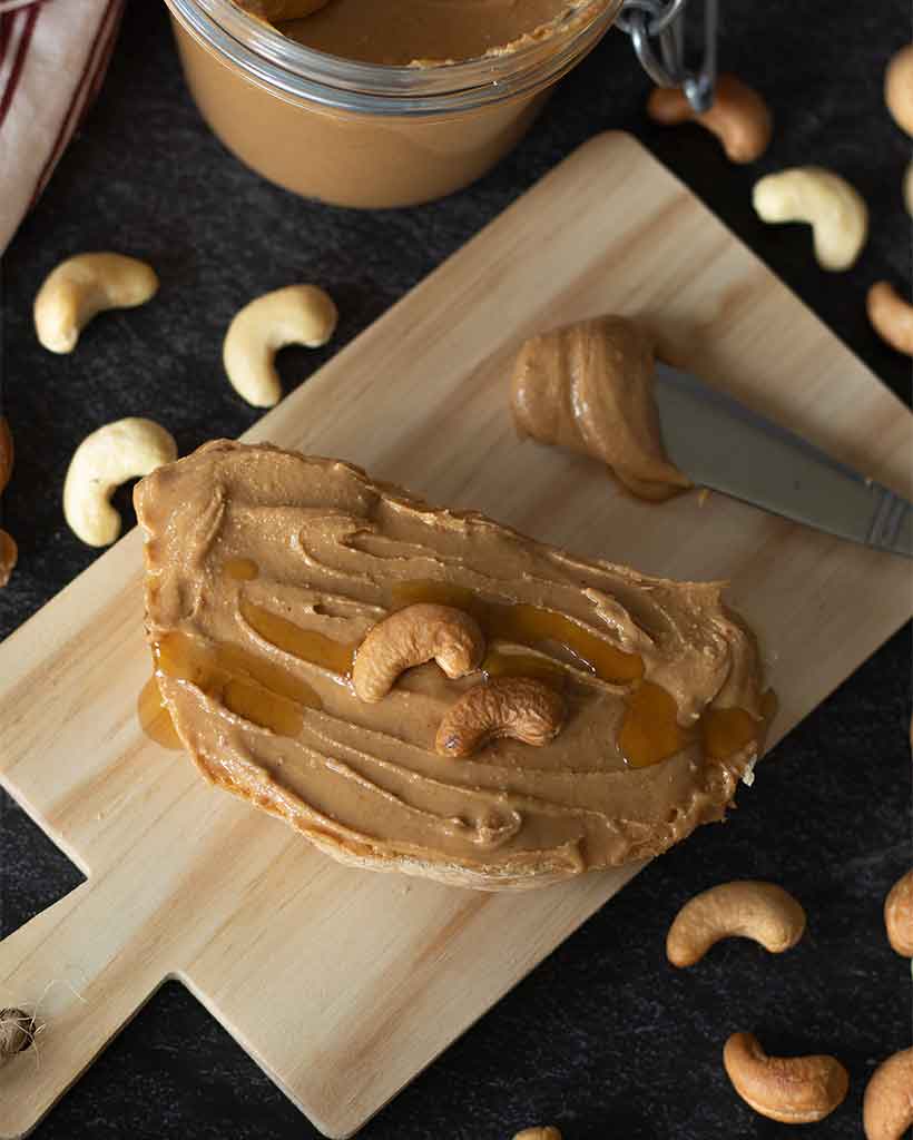 Quick recipe for cashew butter (no oil). Vegan homemade nut butter spreded on a slice of bread on dark background.