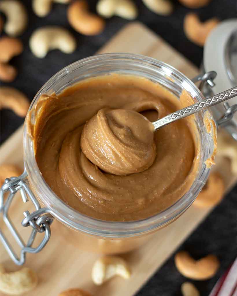 Homemade cashew butter (no oil) in a jar with a spoon. Protein-rich veegan spread for snack or breakfast.