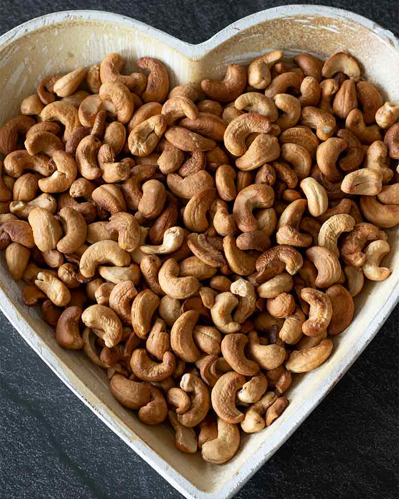 Roasted cashews in a heart-shaped plate on dark background