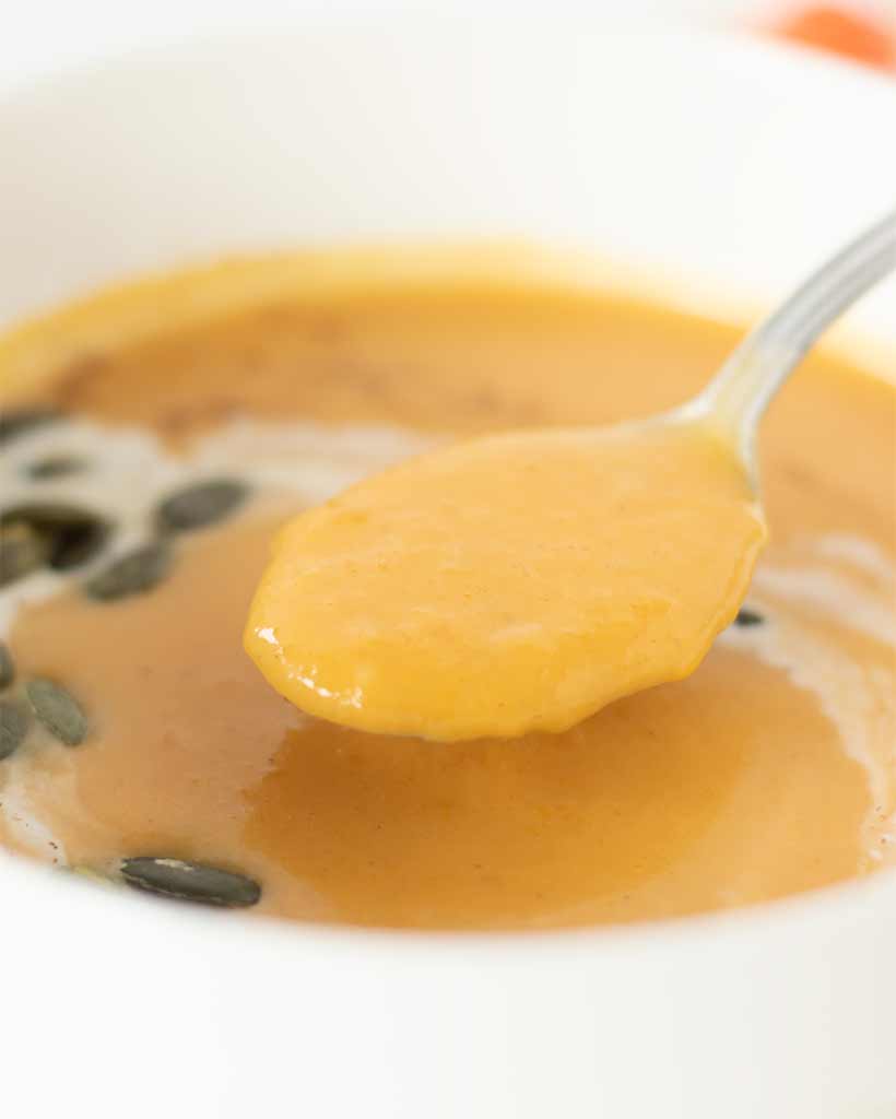 Hearty vegan butternut squash soup with coconut milk and ginger in a spoon over a bowl