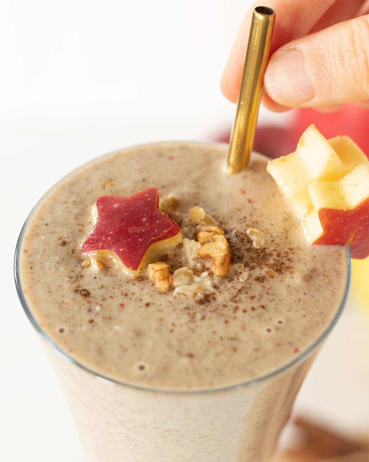 Vegan apple smoothie drink without yogurt (no banana) in a glass decorated with apple stars, chopped walnuts, and cinnamon in a glass with a golden straw