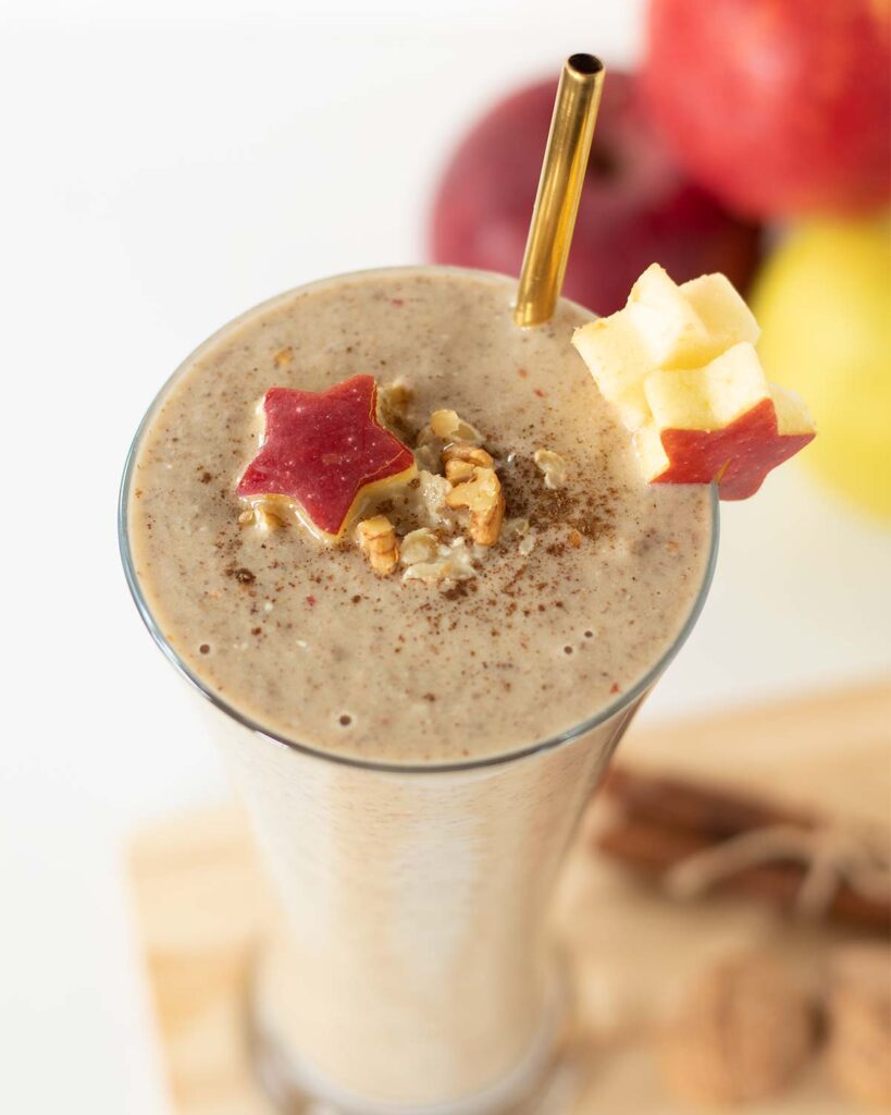 Creamy weight-loss apple peanut butter smoothie shake in a glass decorated with apple stars, cinnamon, and chopped walnuts