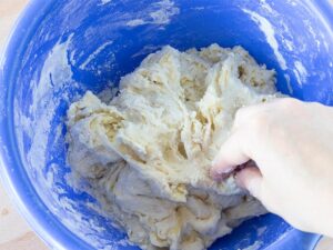 Hand kneading dough in a plastic blue bowl