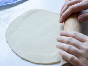 Female hands rolling out dough for tortillas with a wooden rolling pin