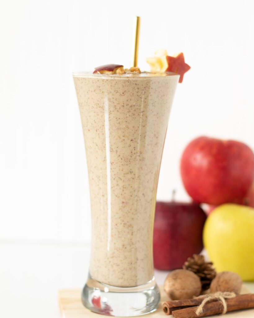Apple pie smoothie without banana or yogurt in a tall glass with golden straw and fresh apples in the background