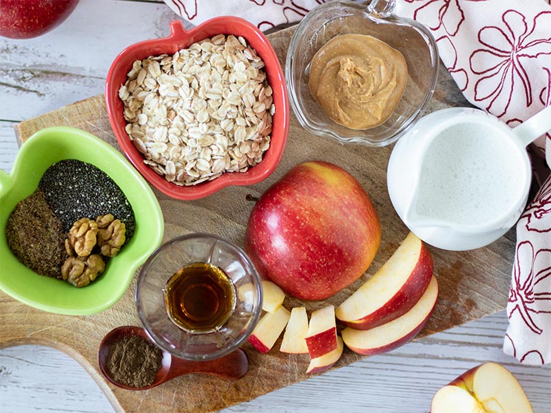 Apple pie overnight oats recipe ingredients: apple, oats, peanut butter, peanut butter, plant-based milk, maple syrup, flaxmeal, cinnamon, and walnuts.