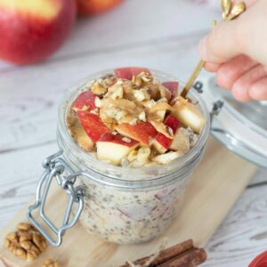 Healthy apple overnight oats without yogurt in a jar with golden spoon in human hand