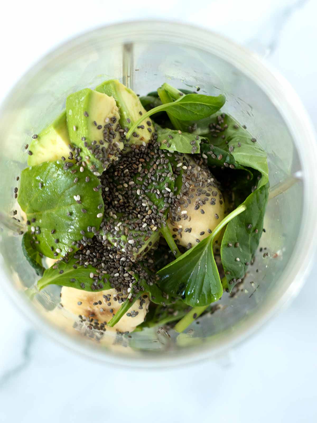 Fresh plant-based ingredients in a blender cup for preparing healthy avocado and banana smoothie