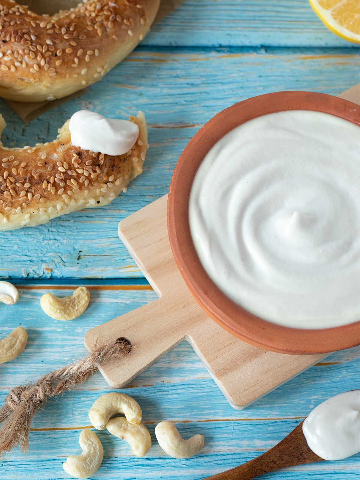 Cashew whole foods sour cream in a bowl with wooden spoon and bagel on table
