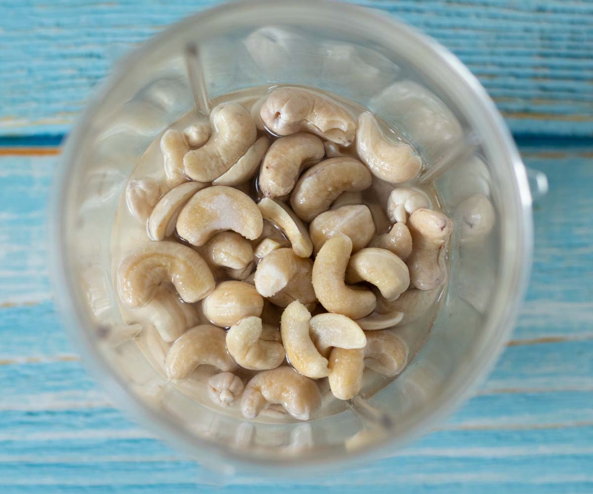 Soaked raw cashews with lemon juice, apple cider vinegar, salt, and water in a blender cup prepared for making vegan sour cream veggie dip