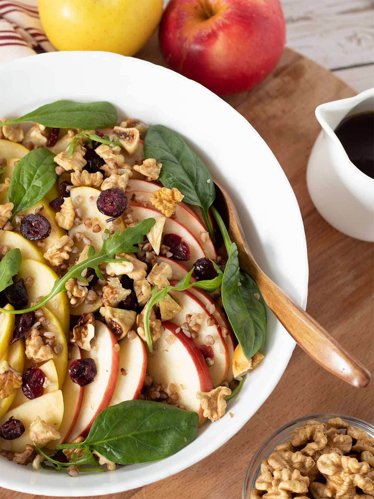Best apple walnut salad in a bowl with fresh greens, dried cranberries, and buckwheat tossed with a homemade cinnamon maple dressing on wooden board