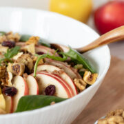 Apple walnut salad with spinach, buckwheat and cranberry in a bowl tossed with homemade vinaigrette in a bowl with wooden spoon
