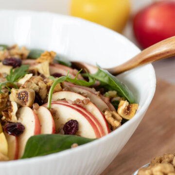 Apple walnut salad with spinach, buckwheat and cranberry in a bowl tossed with homemade vinaigrette in a bowl with wooden spoon
