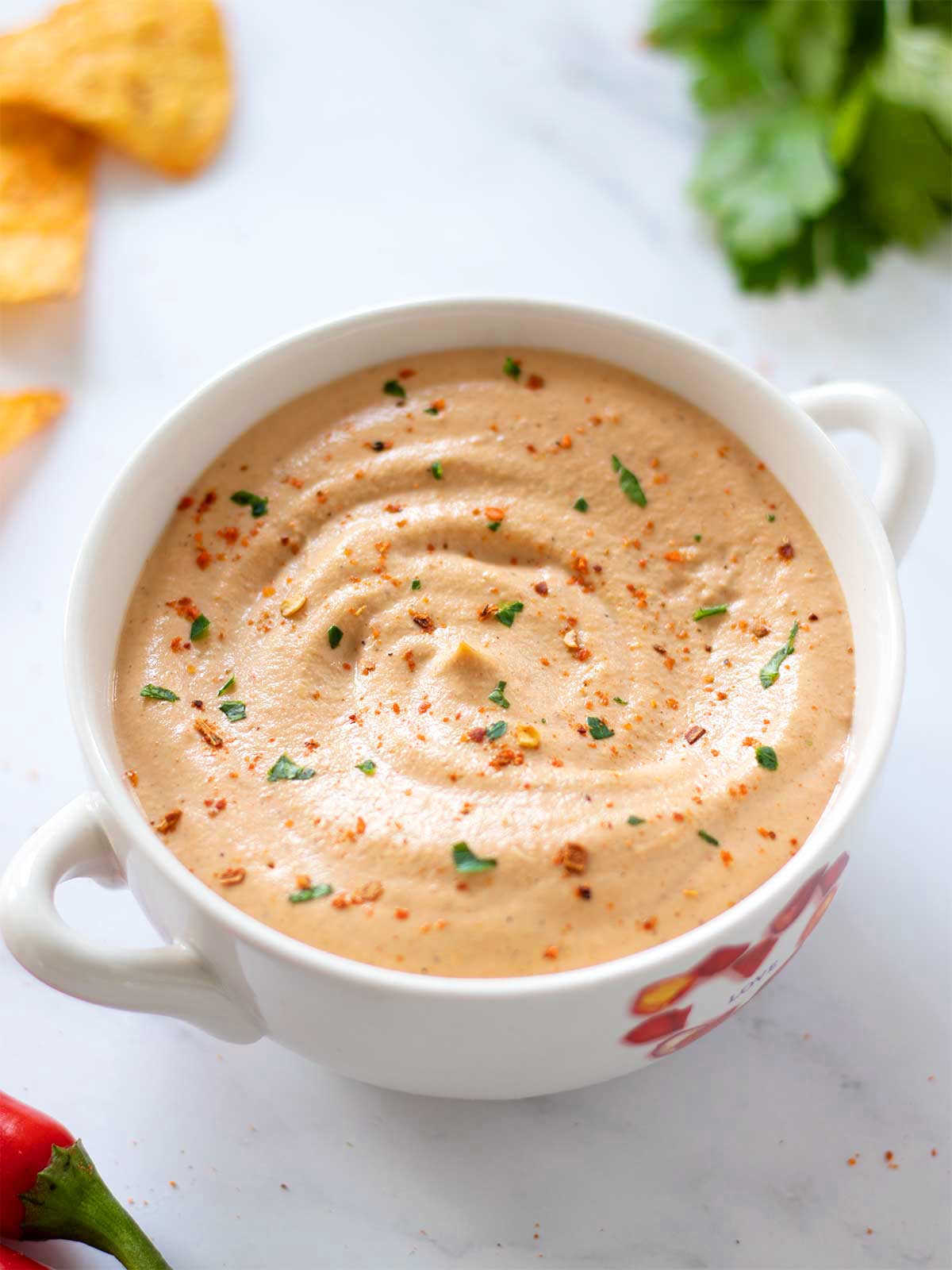 Spicy homemade queso dip made with cashews and whole foods in a bowl topped with red pepper flakes and cholled parsley