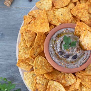 Vegan homemade black bean hummus garnished with red pepper flakes and fresh parsley with corn chips