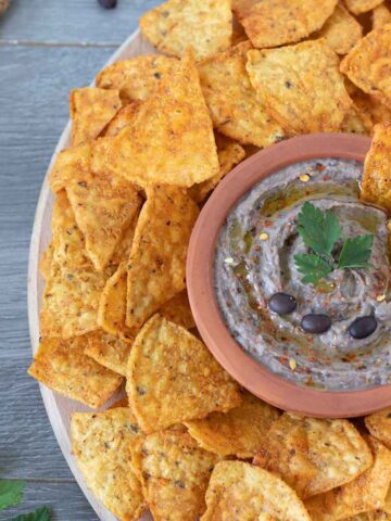Vegan homemade black bean hummus garnished with red pepper flakes and fresh parsley with corn chips