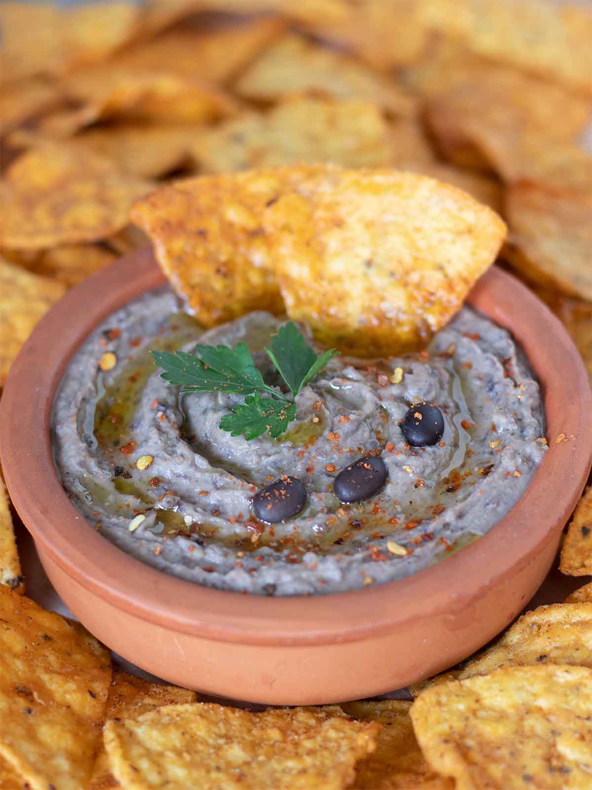 Spicy Mediterranean spread amde from balck beans in a bowl with red paper flakes parsley leaves, and corn chips