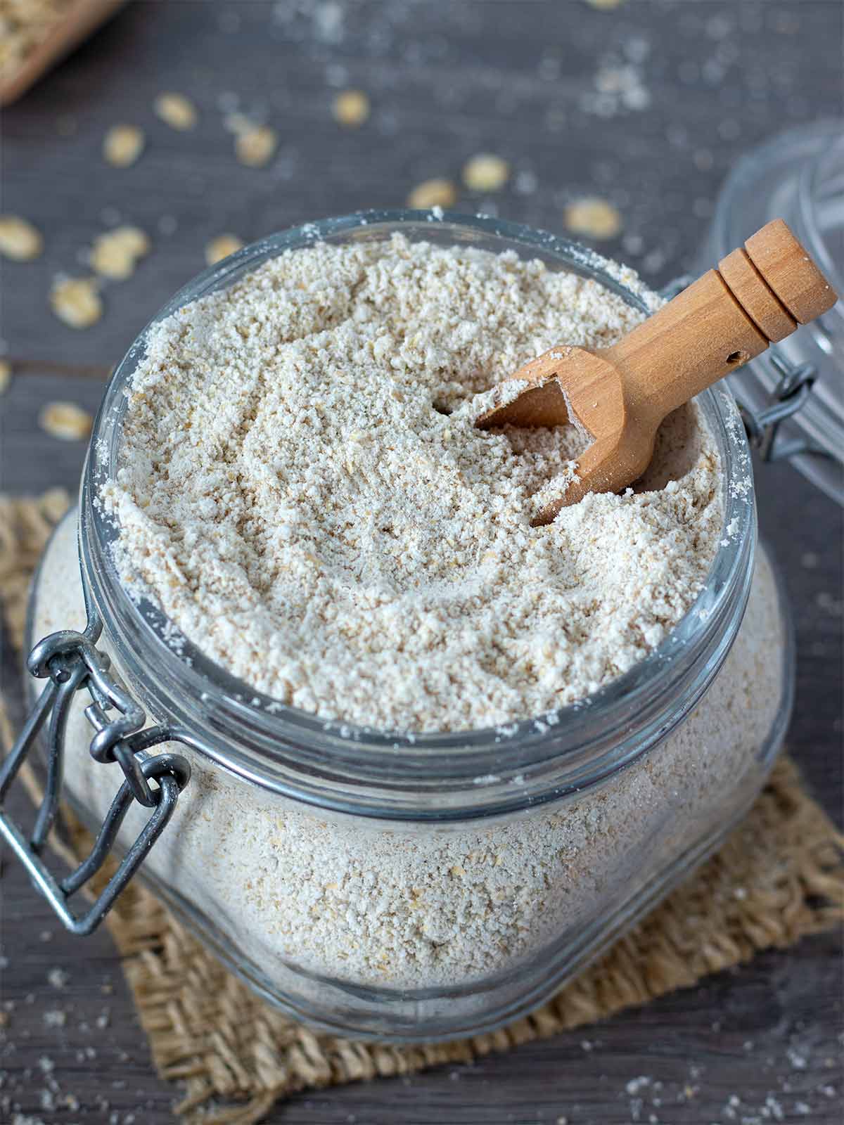 Homemade oat flour made from rolled oats in a glass jar with wooden spoon