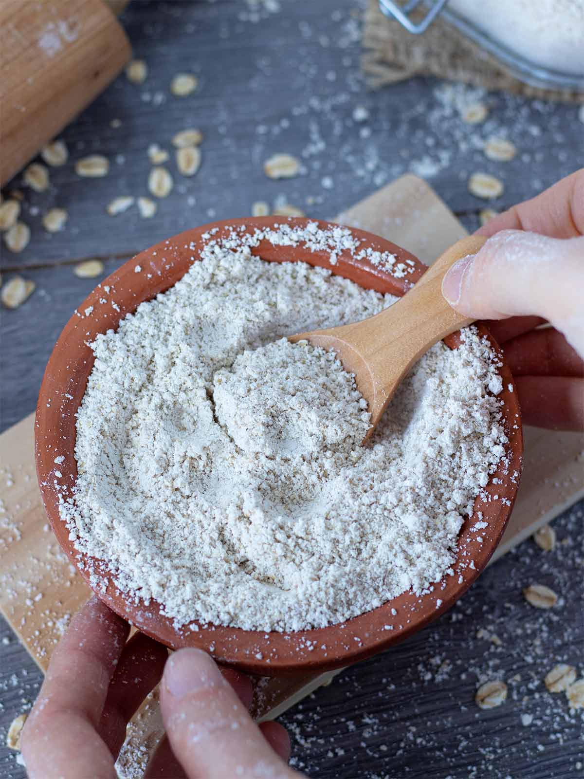 Healthy DIY flour made from rolled oats in a bowl with human hands holding a wooden spoon full of flour