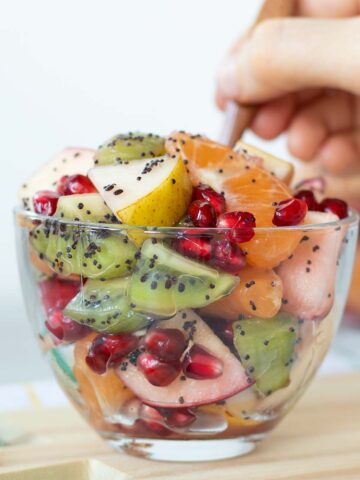 Fresh winter fruit salad with homemade poppy seed dressing in a glass cup with wooden spoon