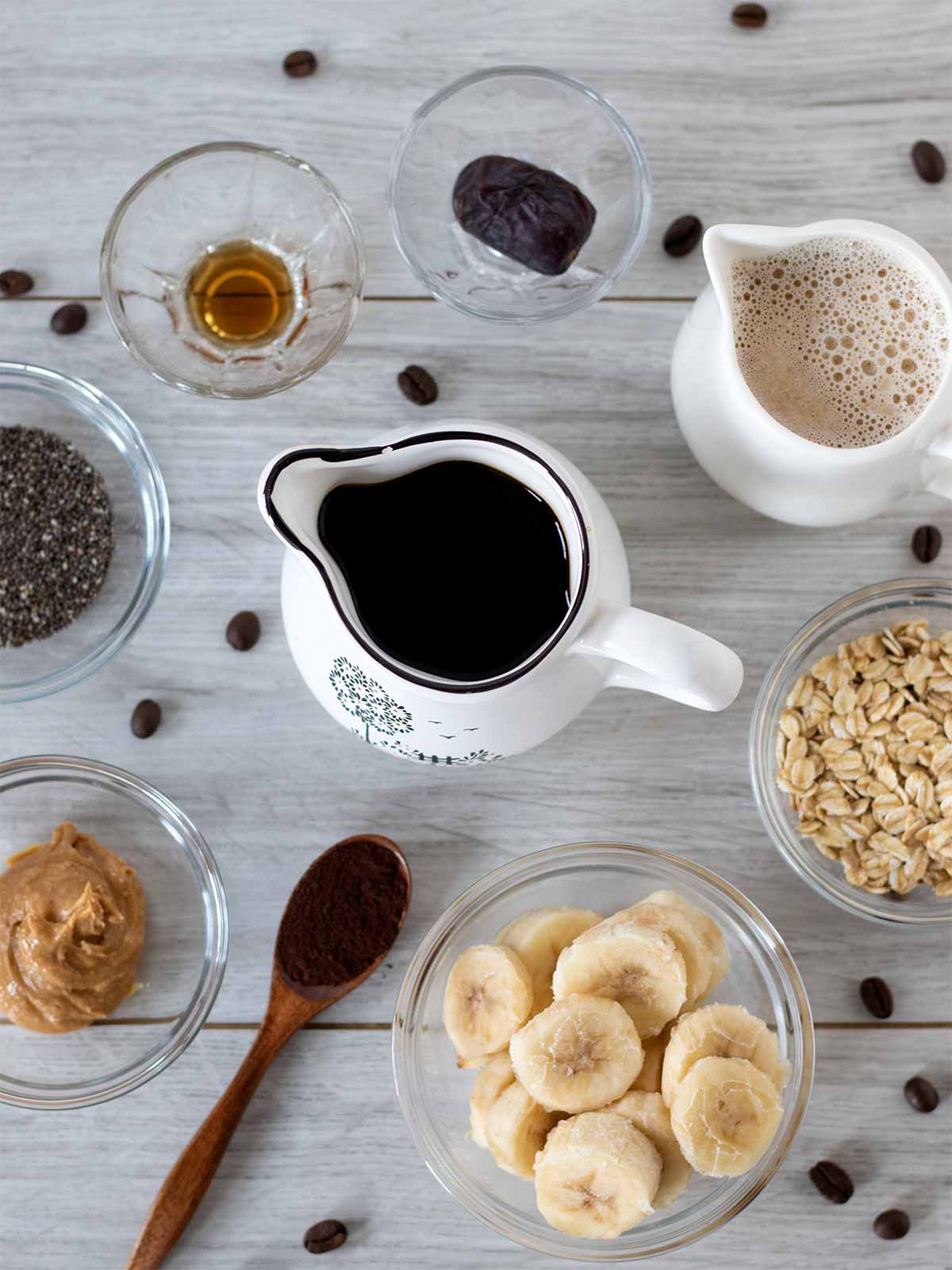 Simple ingredients for making homemade vegan coffee smoothie: brewed coffee, frozen banana, rolled oats, oat milk, peanut butter, chia seeds, cacao powder, pure vanilla eztract, and date.