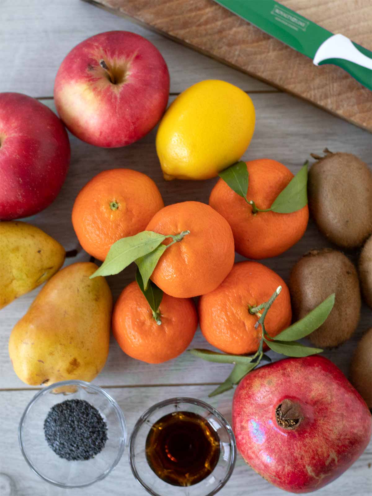 Winter fruit salad ingredients: mandarin oranges, kiwis, apples, pomegranate, pears, lemon, pure maple syrup, and poppy seeds