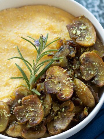 Creamy mushroom polenta dish garnished with fresh rosemary and vegan parmesan cheese for savory breakfast, appetizer, side dish, lunch or dinner