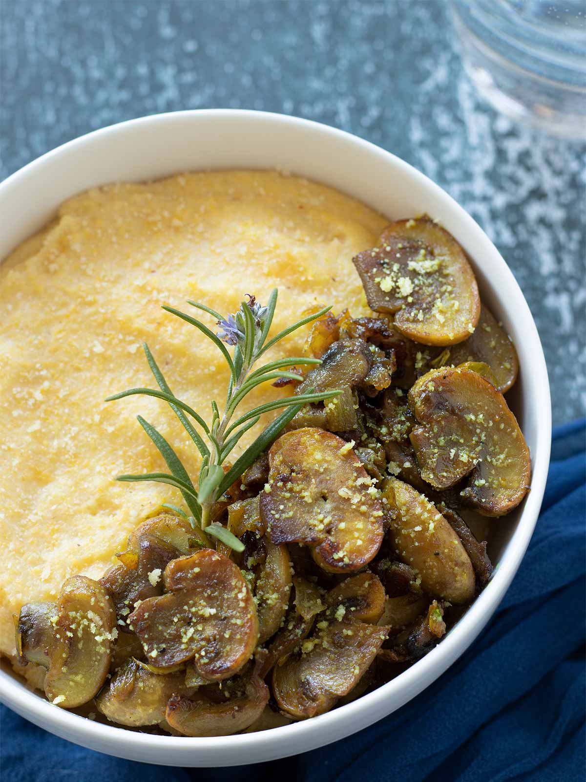 Creamy vegan mushroom polenta dish garnished with fresh rosemary and dairy-free parmesan cheese for savory breakfast, appetizer, side dish, lunch or dinner