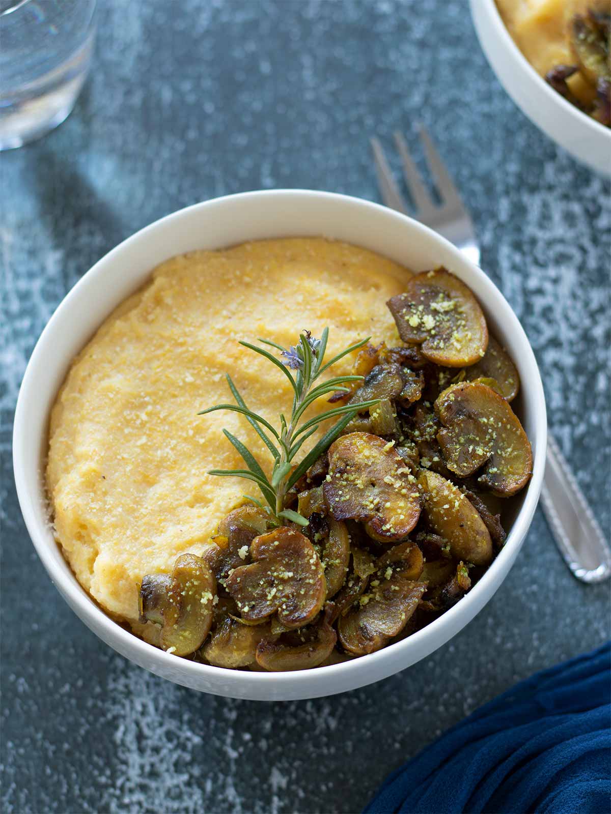 Creamy dairy-free polenta with mushrooms topped with fresh rosemat and vegan parmesan cheese for breakfast, lunch, or dinner